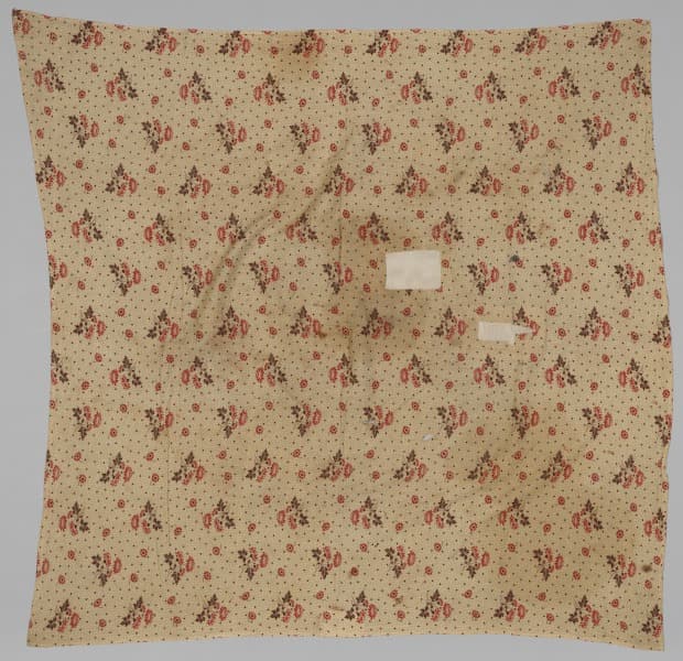 Aged cream-colored cotton wrapping cloth patterned with reddish and dark floral clusters, shown laid flat.