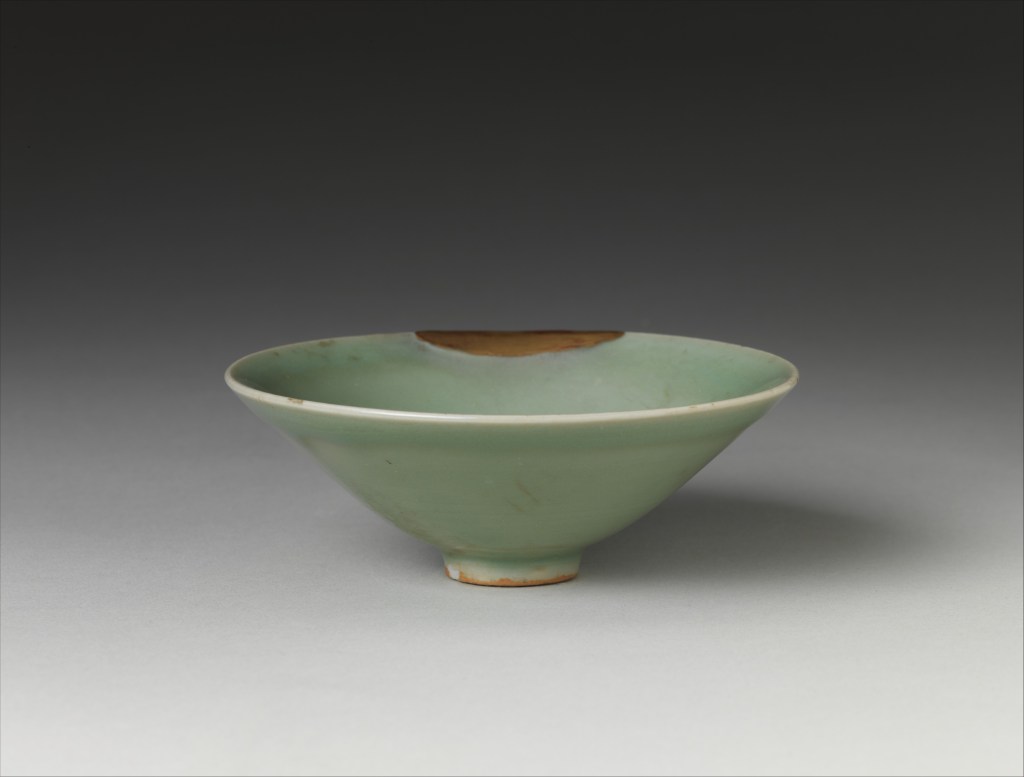 Pale green celadon tea bowl in an angled side view, with a broad gold-brown repair visible along the far rim.