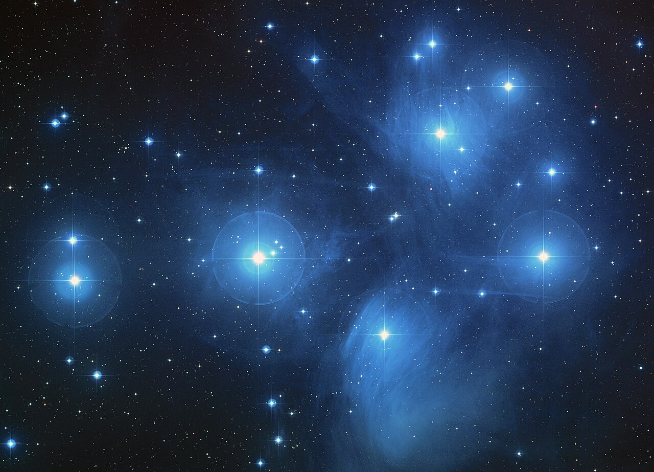 Bright stars of the Pleiades cluster surrounded by blue nebulosity.